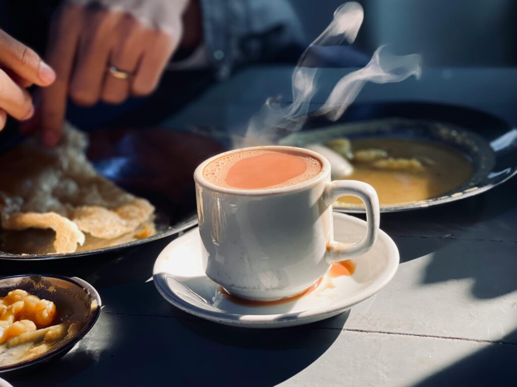 A steaming cup of tea on a table set with breakfast dishes, captured in morning light.